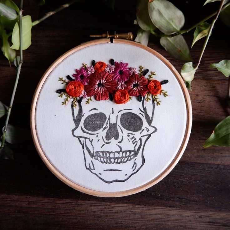 a cross stitch skull with flowers in it's hair on top of a wooden table