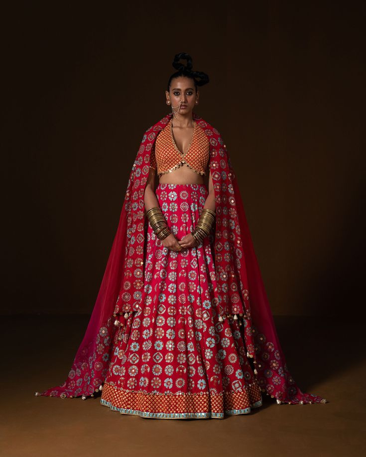 ANARDANA LEHNGA : this lehnga is made in a plush summer silk with 12 kind of flowers printed all over the base, placed in a geometric manner, and is bound with an intricate geometric border. Its hand embroidered in small mirror and sequin embroidery . The blouse is printed in small geometric pattern, then embridered with square shape sequin . Ombre Dupatta is printed and embroidered on borders and has metal coin hanging detail. Fabric : summer silk and organza fuchia -red ombre Color 15 DAYS Del Traditional Sets With Geometric Embroidery For Transitional Season, Traditional Sets With Geometric Embroidery For Festivals, Traditional Geometric Embroidered Sets For Festivals, Fitted Traditional Wear With Geometric Embroidery For Transitional Season, Fitted Traditional Wear With Geometric Embroidery, Traditional Geometric Embroidery Sets For Festivals, Diwali Traditional Wear With Geometric Embroidery, Festive Diwali Set With Geometric Embroidery, Festive Sets With Geometric Embroidery For Diwali