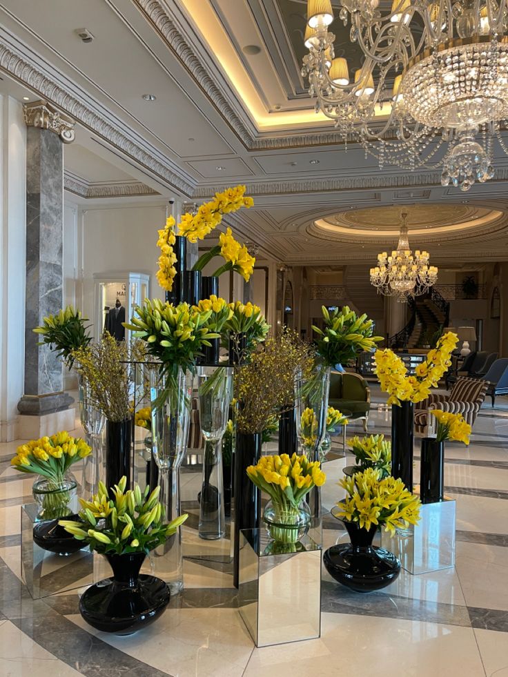 a bunch of vases filled with yellow flowers on top of a white marble floor