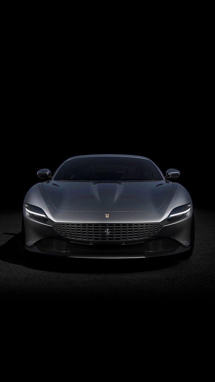 the front end of a silver sports car on a dark surface with its lights on