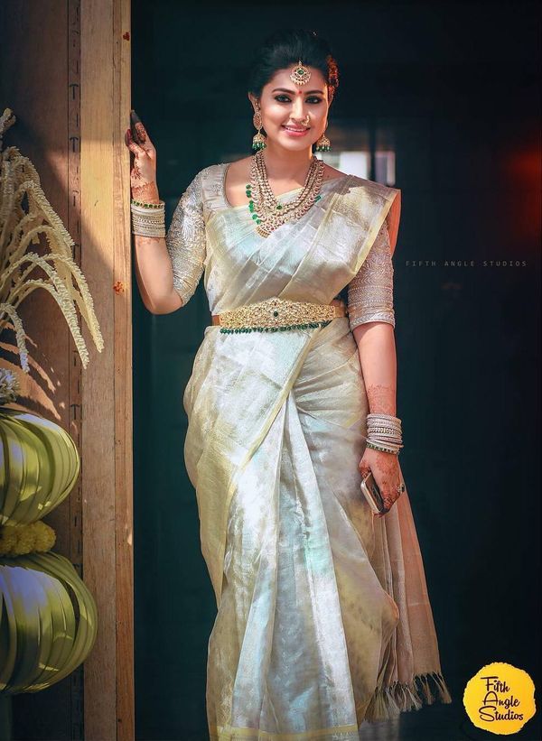 a woman in a white sari and gold jewelry is posing for the camera with her hand on her hip