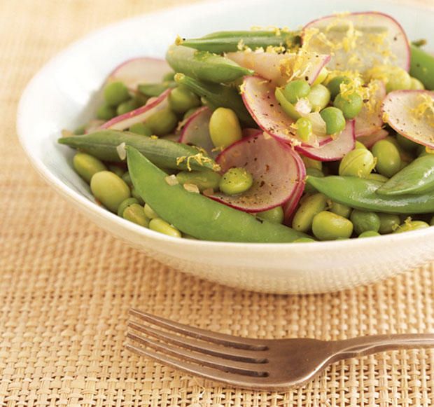 a white bowl filled with peas and radishes on top of a table next to a fork