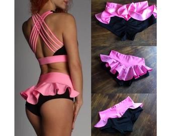 a woman in black and pink swimsuit with ruffles on the bottom, standing next to a wooden floor