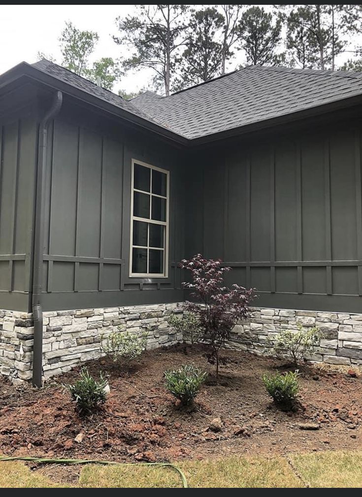 the front of a house that has been painted dark green and is surrounded by landscaping