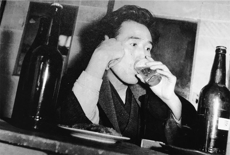 a man sitting at a table eating a sandwich and drinking from a wine bottle in front of him