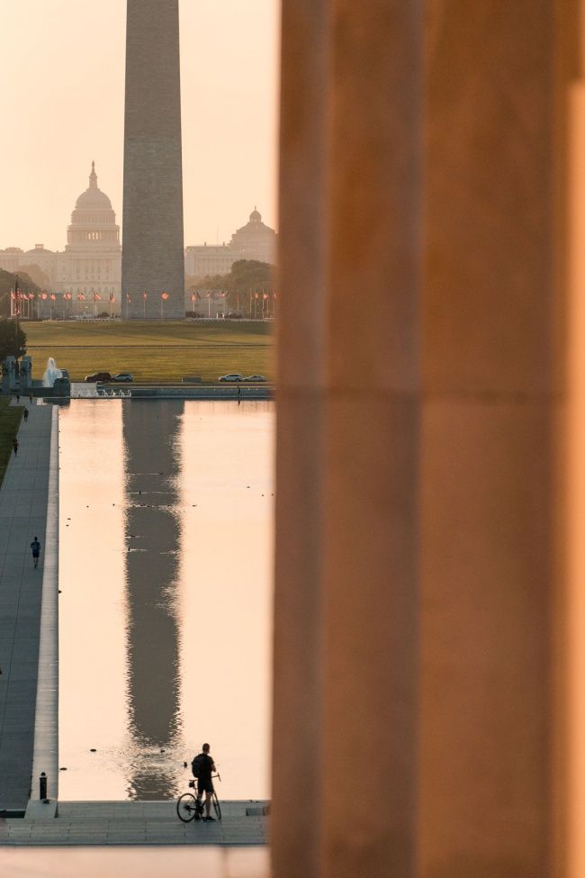 a person riding a bike near the washington monument and reflecting in the water at sunset