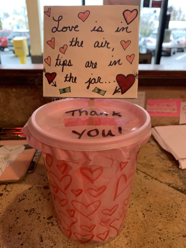 a plastic cup with writing on it and a note attached to the lid that says love is in the air, tips are in the jar