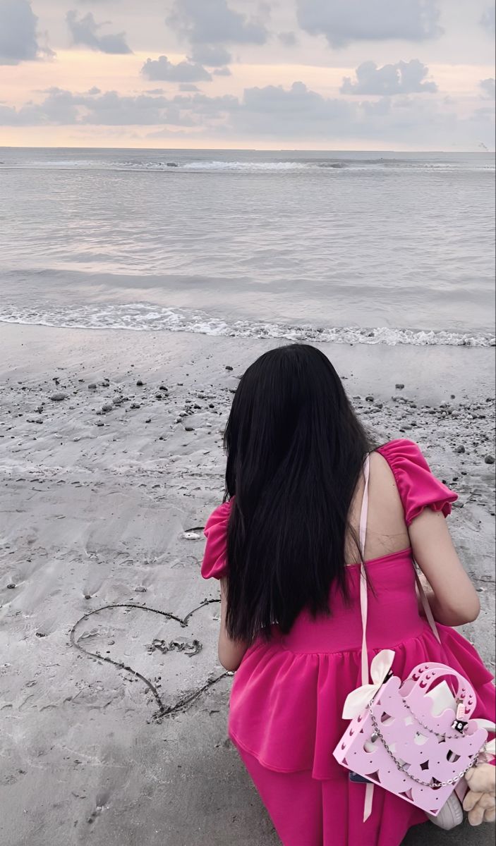 a woman sitting on the beach with her back to the camera, looking out at the ocean