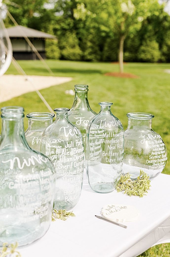 several glass bottles with writing on them sitting on a white table in the middle of a grassy area