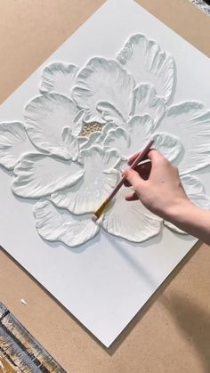 a person is painting a flower on a piece of white paper with a brush in their hand