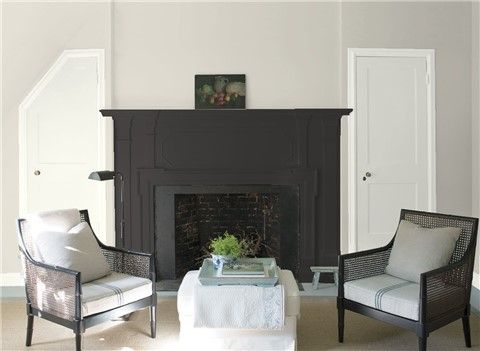 a living room with two chairs and a table in front of a fire place that has a painting on the wall