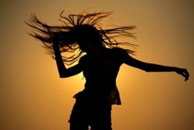 the silhouette of a woman with her hair blowing in the wind as the sun sets