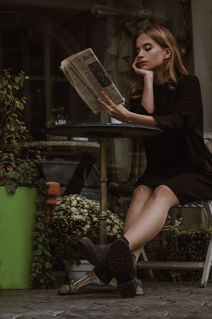 a woman is sitting at a table reading a newspaper and looking down on her knee