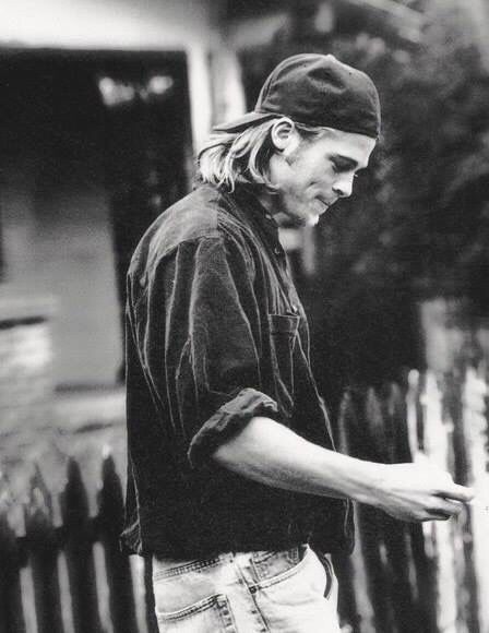 a man standing in front of a fence with his hand on the handle of a skateboard