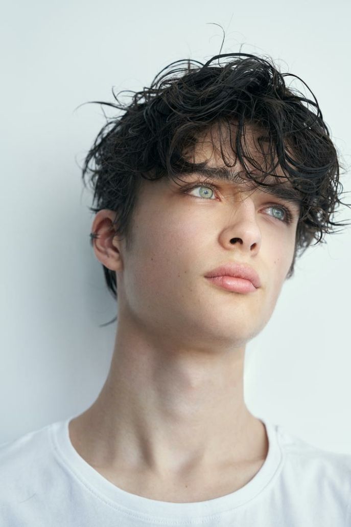 a young man with curly hair is looking at the camera while wearing a white t - shirt