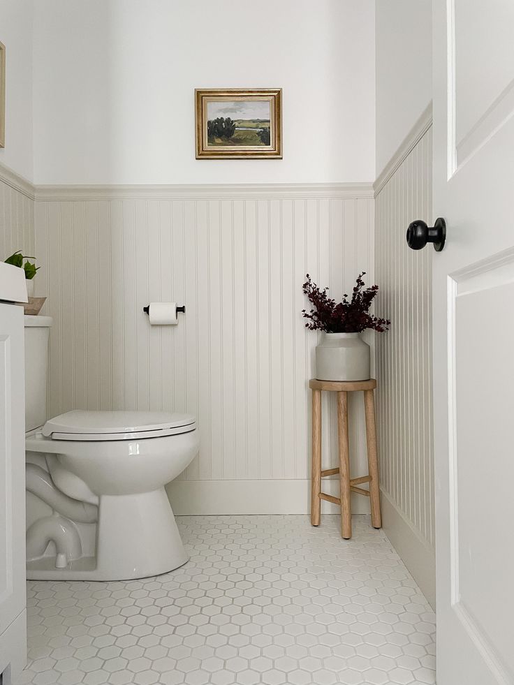 a white toilet sitting in a bathroom next to a wooden stool with flowers on it