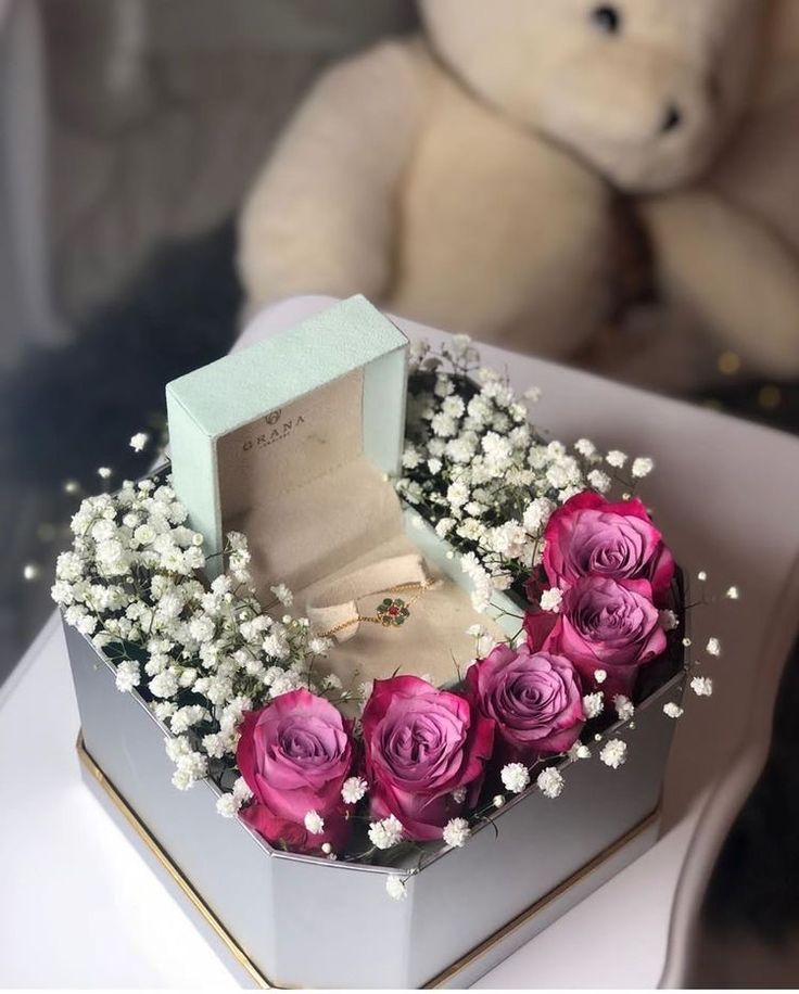 a white box with pink roses and baby's breath sits next to a teddy bear