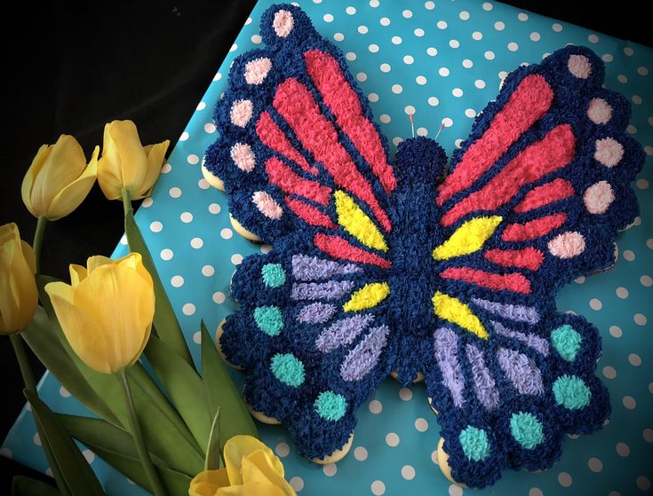 a crocheted butterfly sitting on top of a table next to yellow tulips