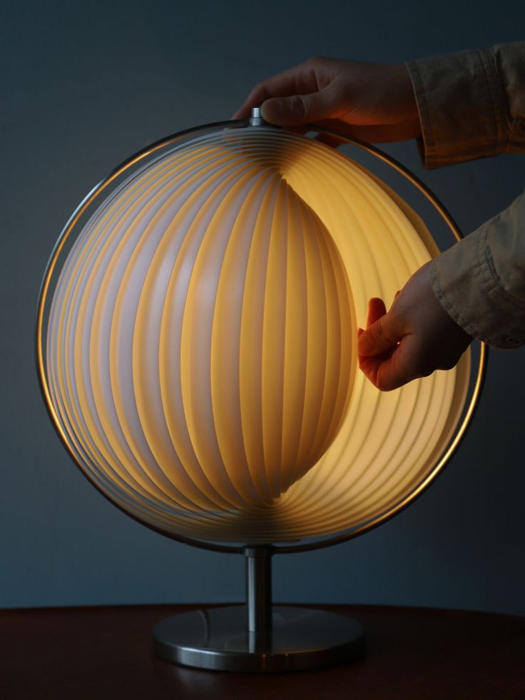 a person's hand is touching the light on a globe shaped table top lamp