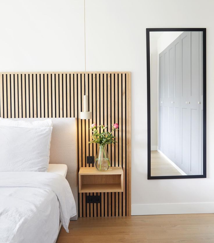 a white bed sitting next to a tall mirror on top of a wooden headboard