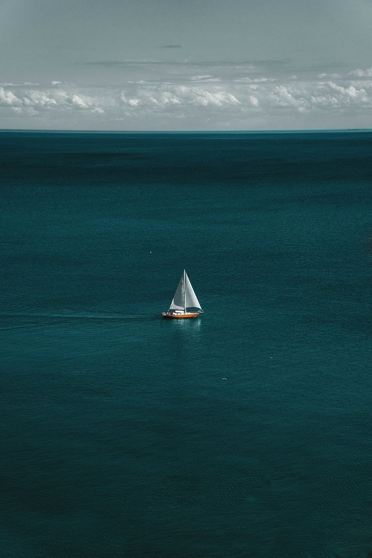 a sailboat floating in the middle of an ocean with blue water and white clouds