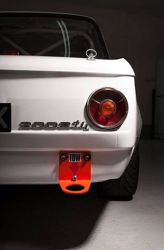 the back end of a white sports car with an orange light on it's license plate