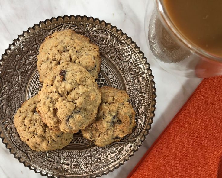 three cookies on a plate next to a cup of tea and an orange napkin with a red cloth