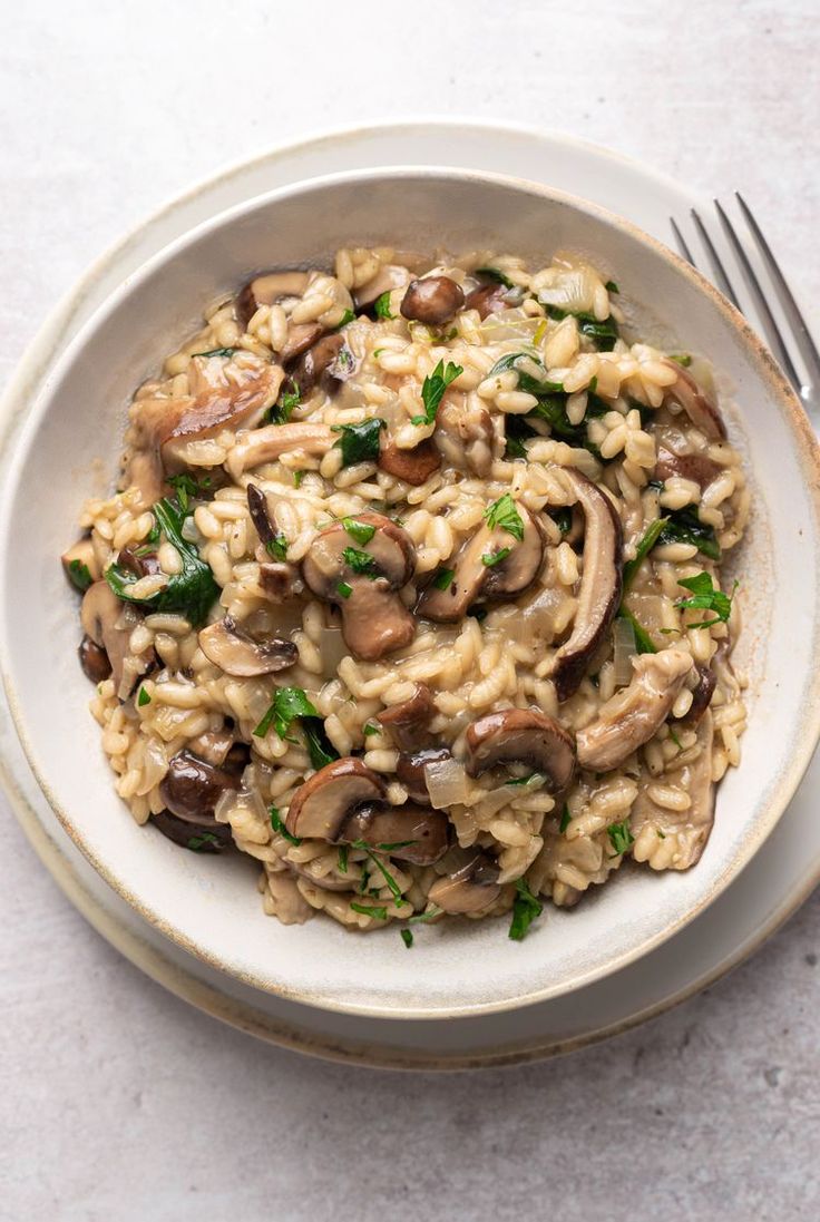 a white bowl filled with pasta and mushrooms on top of a table next to a fork