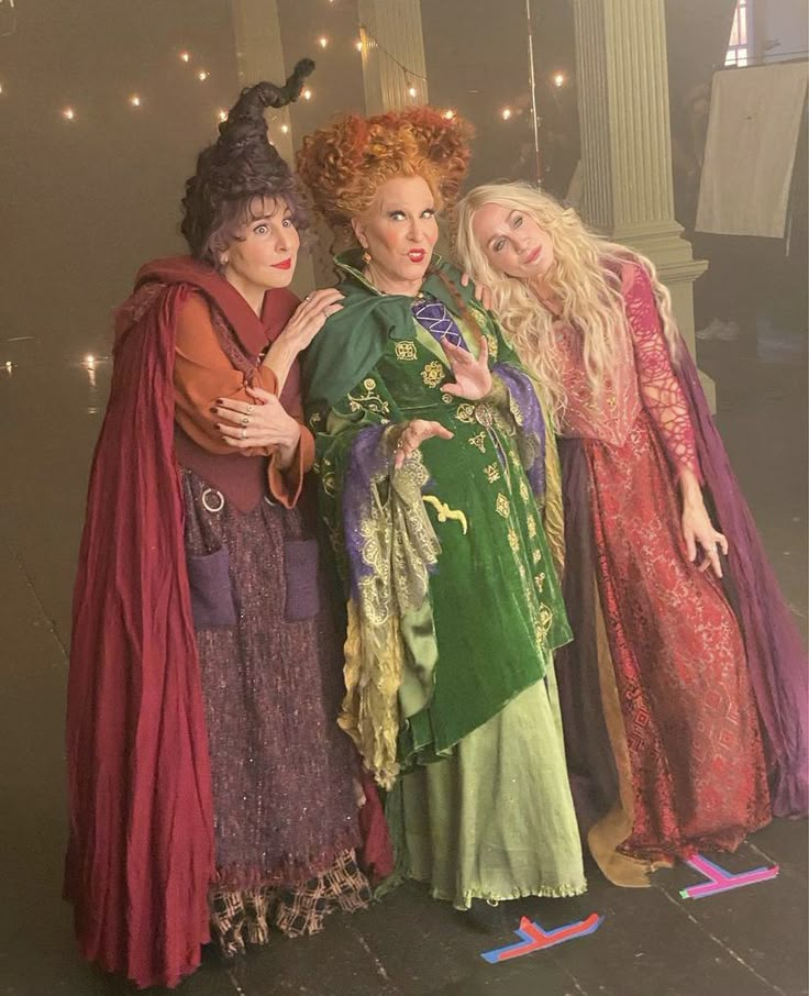 three women dressed up in costumes posing for a photo with lights on the wall behind them