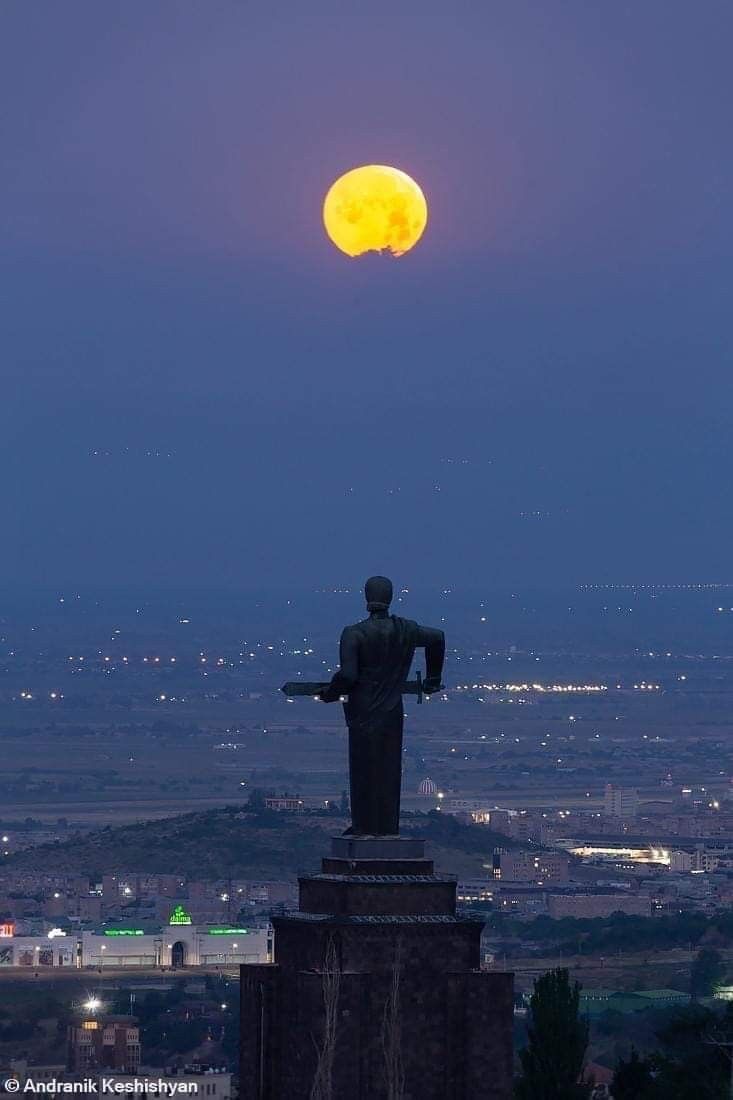 the full moon is seen behind a statue on top of a hill