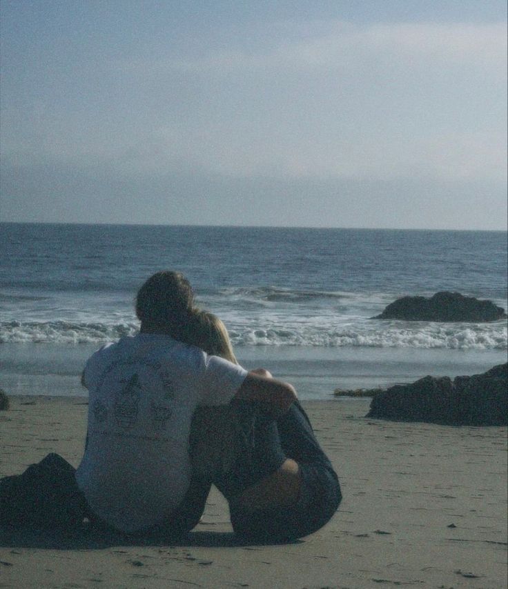 two people sitting on the beach looking out at the ocean