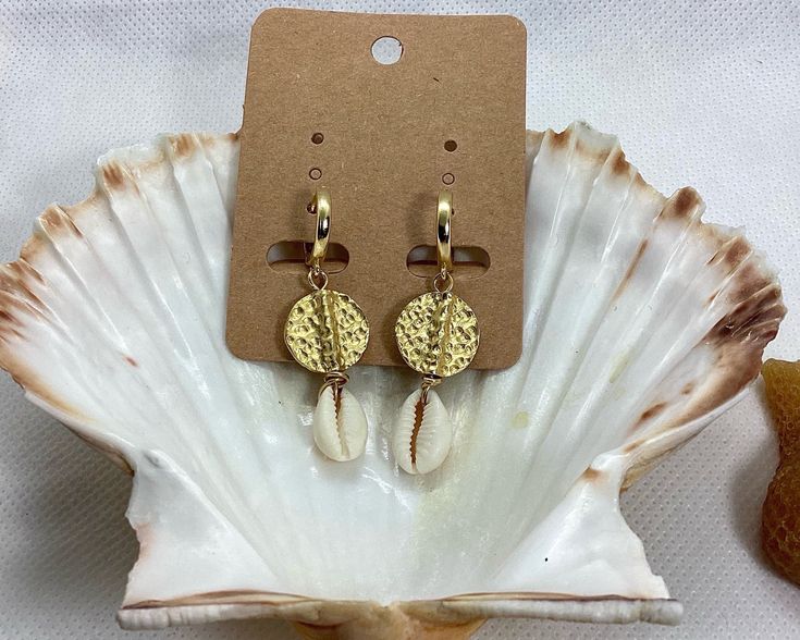 Elevate your beach style with these stunning Hammered Disc and Cowrie Shell Earrings. This beautiful pair is handcrafted with gold plated brass disc beads and natural cowrie shells, making them versatile enough to wear every day and suitable for any occasion. The lightweight design and easy to wear leverback hoops make them a comfortable choice for all-day wear. The earrings measure 5 cm in length, with the 24K gold plated hoops measuring 15 mm in diameter and 1.6 cm in length. These statement e Gold Small Hoop Jewelry For The Beach, Gold Dangle Earrings For Beach Season, Handmade Dangle Hoop Earrings For Vacation, Handmade Small Hoop Earrings For Vacation, Gold Hoop Jewelry For Vacation, Handmade Small Hoop Jewelry For Vacation, Handmade Round Hoop Earrings For Beach, Handmade Hoop Earrings For The Beach, Handmade Round Hoop Earrings For Vacation