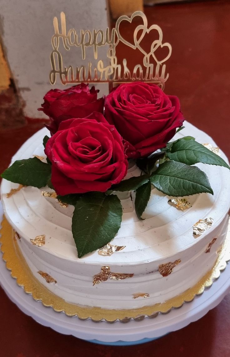 two roses on top of a cake with the words happy anniversary written in gold lettering