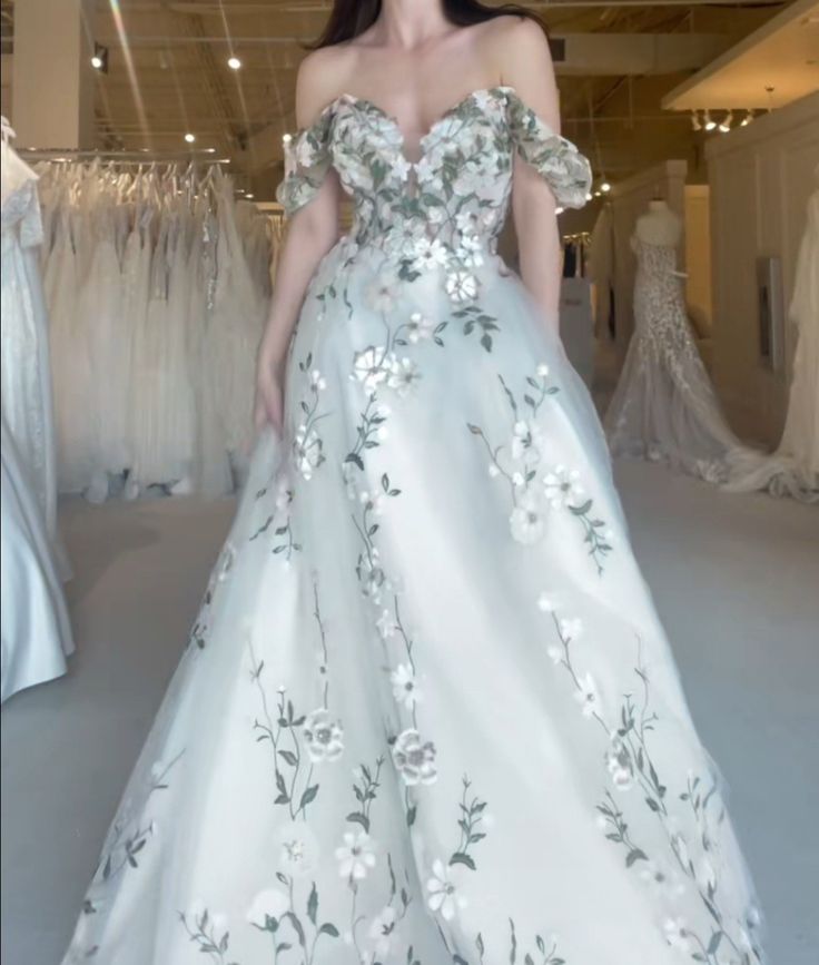 a woman standing in front of a white dress with floral appliques on it