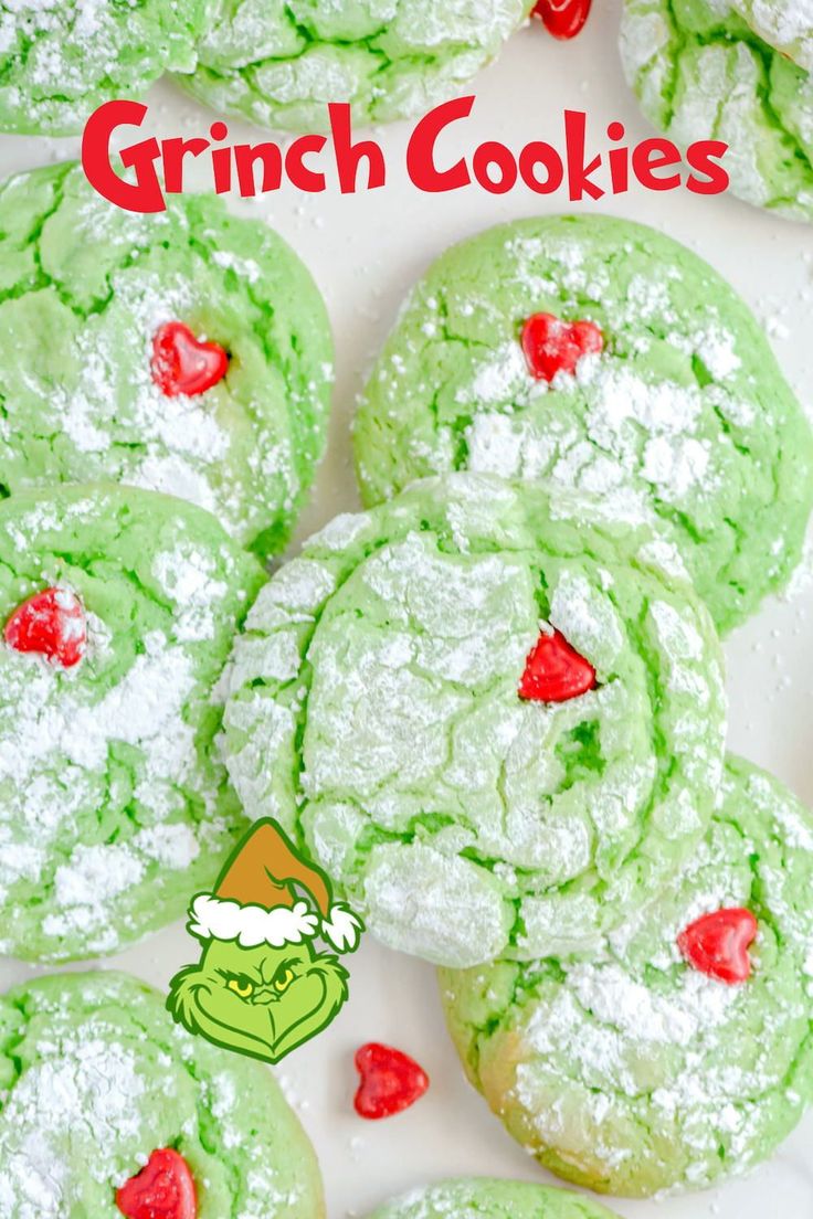 green christmas cookies with white powdered sugar on top and red candy hearts in the middle