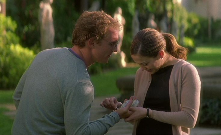 a man and woman standing next to each other looking at something on the ground in front of them