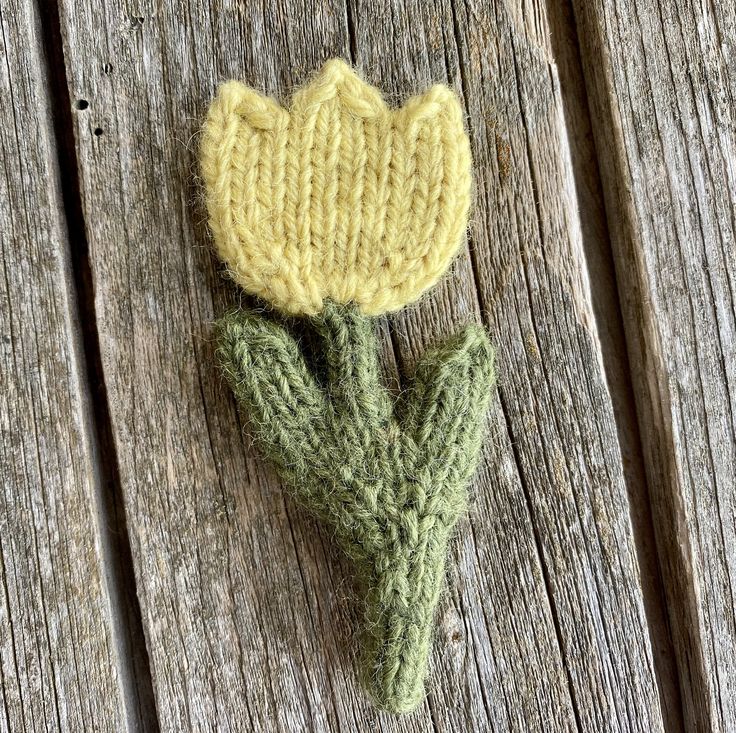 a knitted flower sitting on top of a wooden table next to a piece of wood