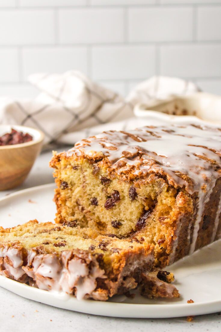 a loaf of chocolate chip banana bread on a white plate with a bowl of cranberries in the background