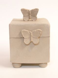 a small white box with a butterfly decoration on the top and bottom, sitting in front of a white background