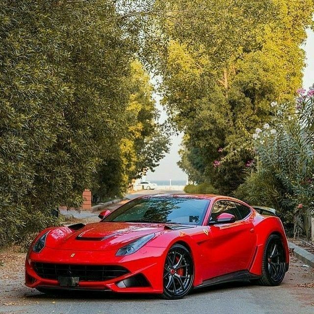 a red sports car parked on the side of a road next to trees and bushes