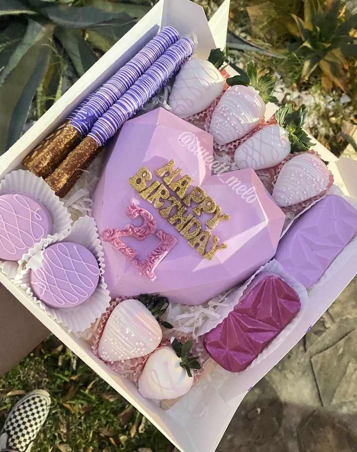 a pink heart shaped box filled with cupcakes and other desserts next to succulents