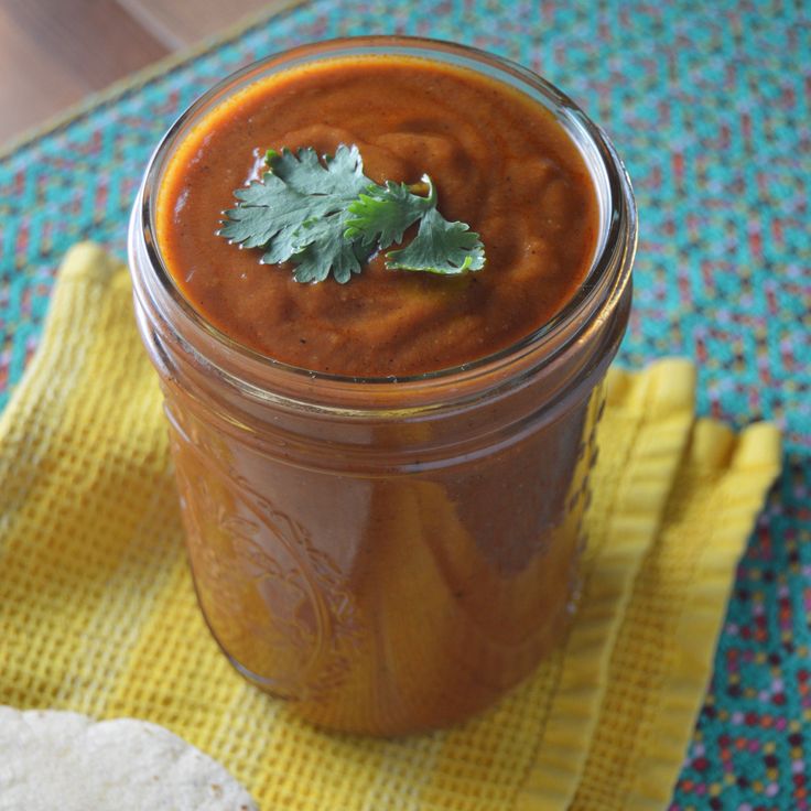 a jar filled with red sauce and garnished with cilantro on a yellow napkin