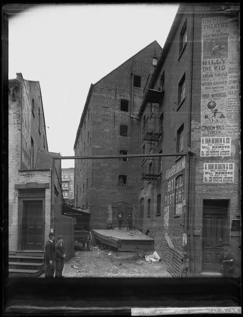 an old black and white photo of people standing in front of some buildings with signs on them