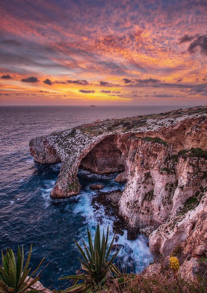 the sun is setting over an ocean cliff