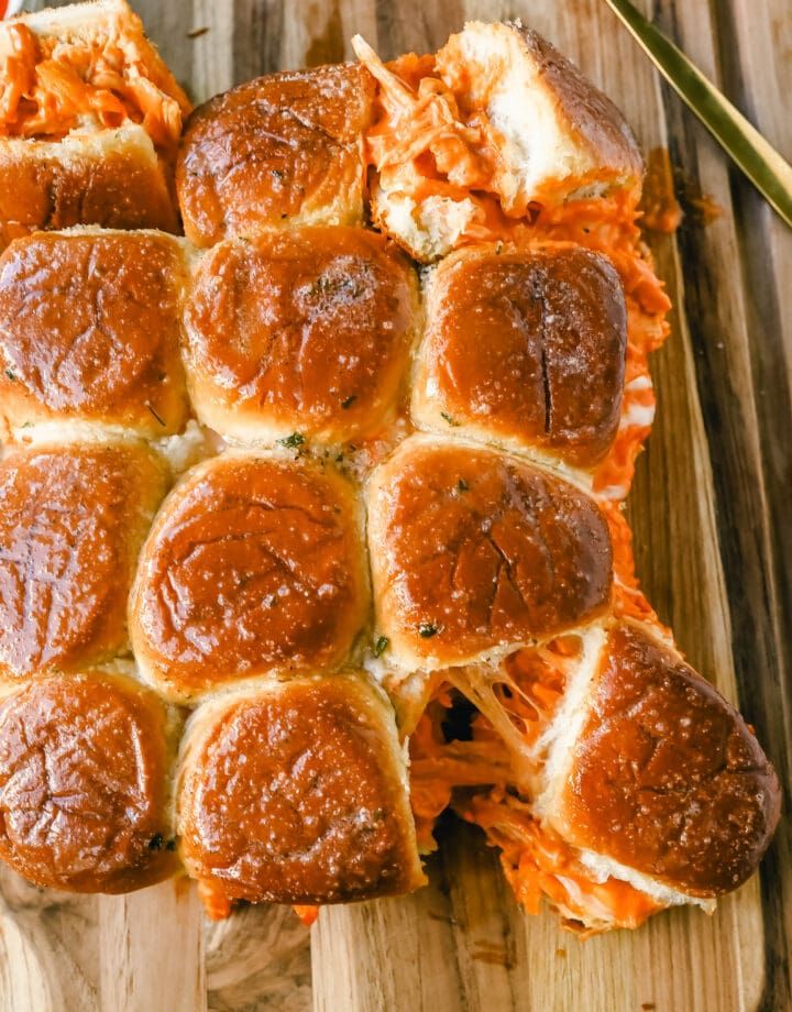 a wooden cutting board topped with rolls covered in cheese