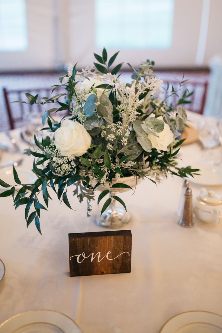 a centerpiece with white flowers and greenery sits on top of a round table