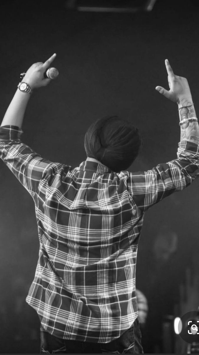 a man in plaid shirt standing on stage with his arms up and hands raised to the side