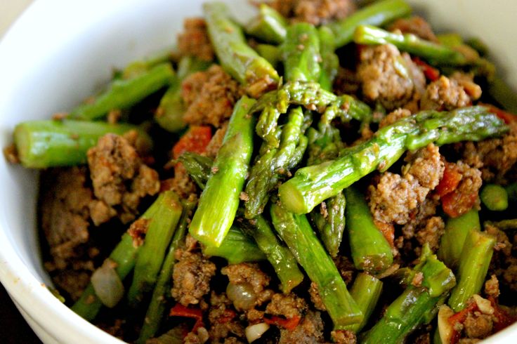 a white bowl filled with meat and asparagus