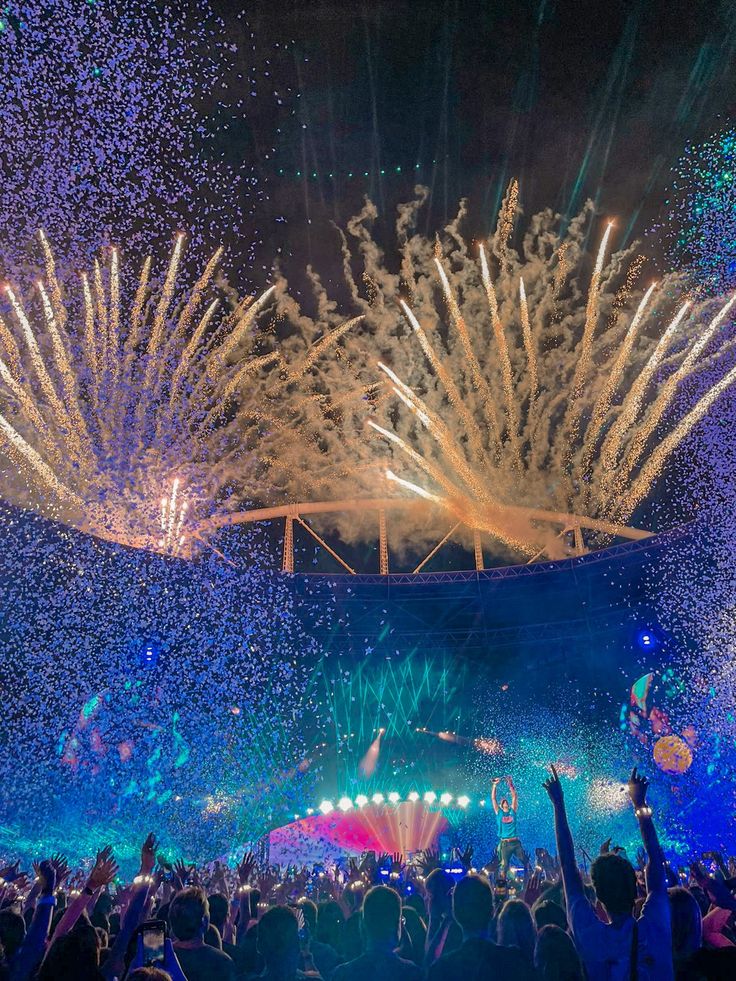 fireworks and confetti fill the night sky above an outdoor concert