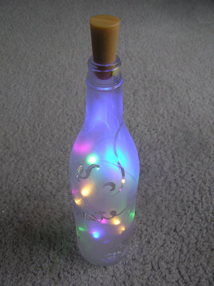 a bottle with some lights in it on the floor next to a corkscrew